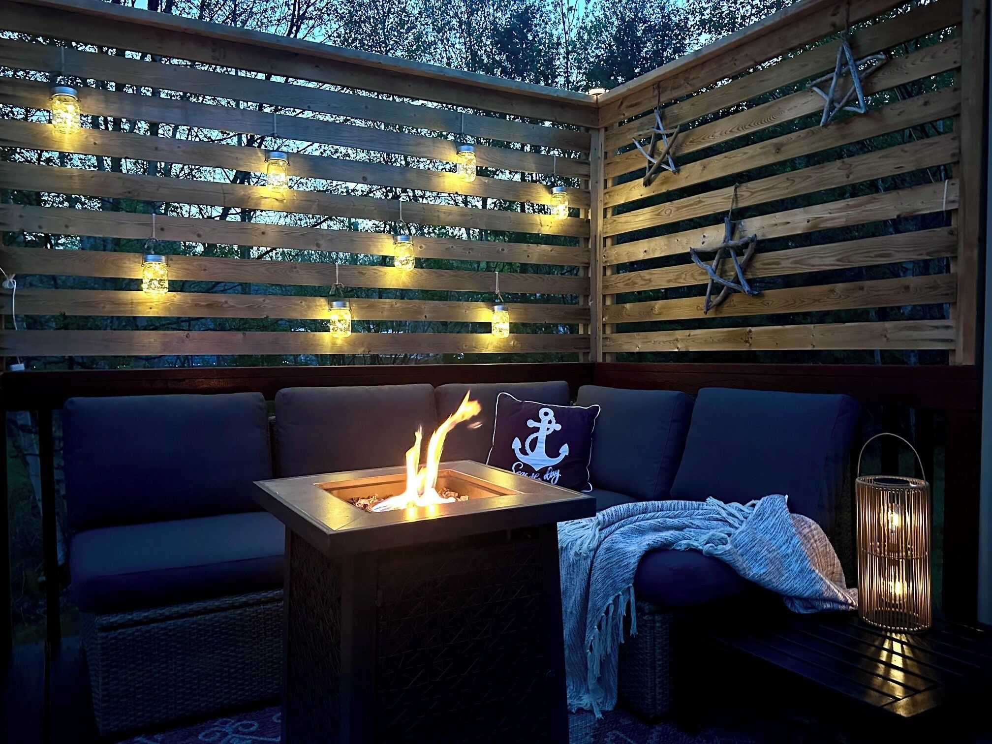 A wooden deck with a fire pit, seating, and string lights.
