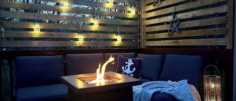 A wooden deck with a fire pit, seating, and string lights.