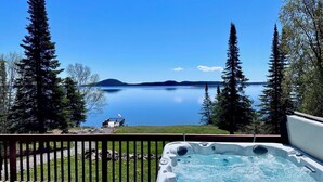 A hot tub on a deck with a view of a calm lake and distant mountains.