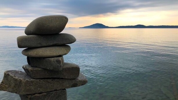 A stack of stones by a calm body of water with a distant mountain and cloudy sky.