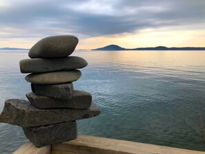 Una pila de piedras junto a un cuerpo de agua tranquilo, con una montaña distante y cielo nublado.