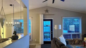 A living room with a ceiling fan, a chandelier, a sofa, and a large window with blinds.