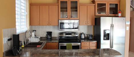 A kitchen with wooden cabinets, a stainless steel refrigerator, a microwave, and a stove.