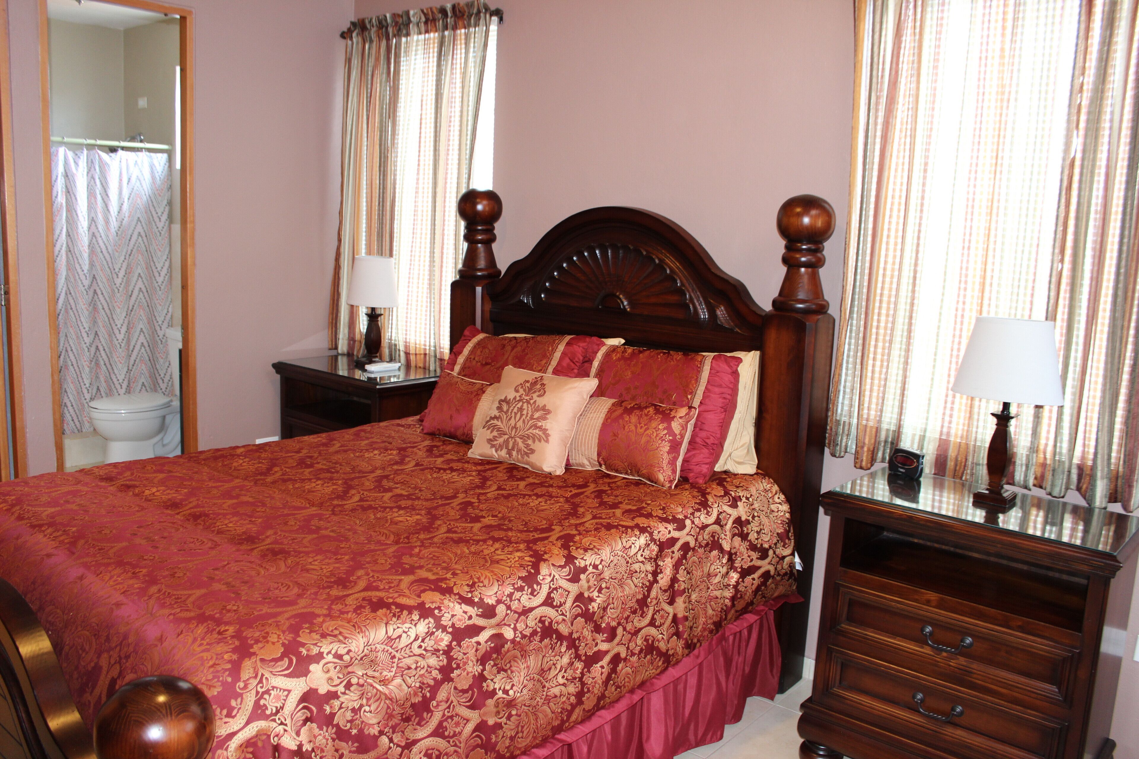 A neatly made bed with a red and gold patterned bedspread, a wooden headboard, and two bedside tables with lamps.
