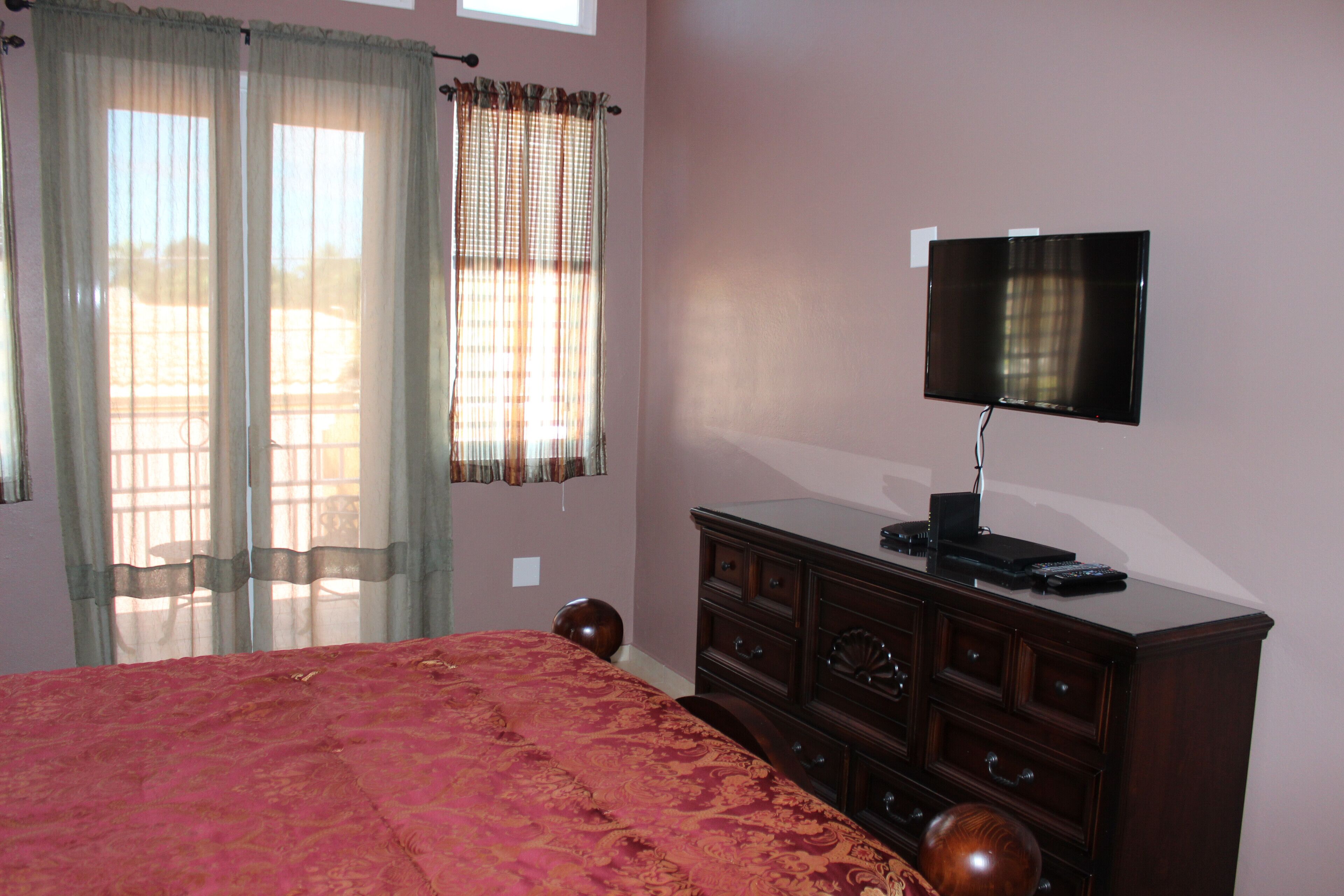 A bedroom with a bed, a dresser, a television, and a window with curtains.