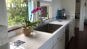 A kitchen with a white countertop, a sink, and a window with a view of greenery.