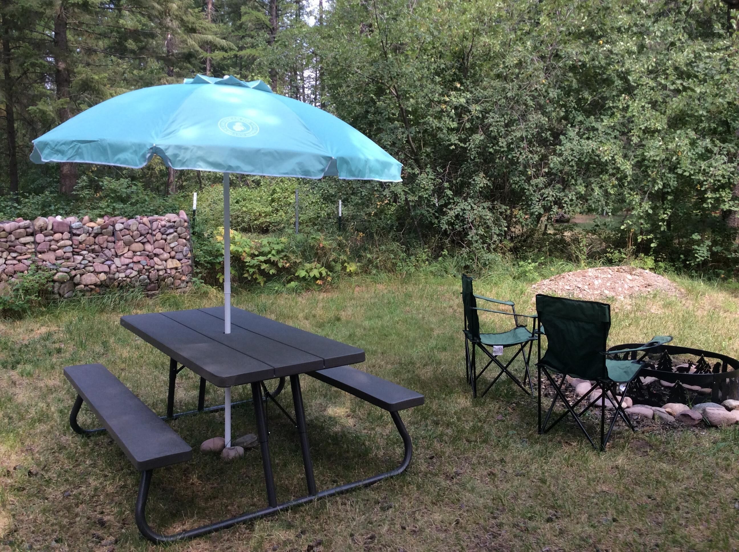 An outdoor picnic setup with a table and benches, a folding chair, and a blue umbrella.