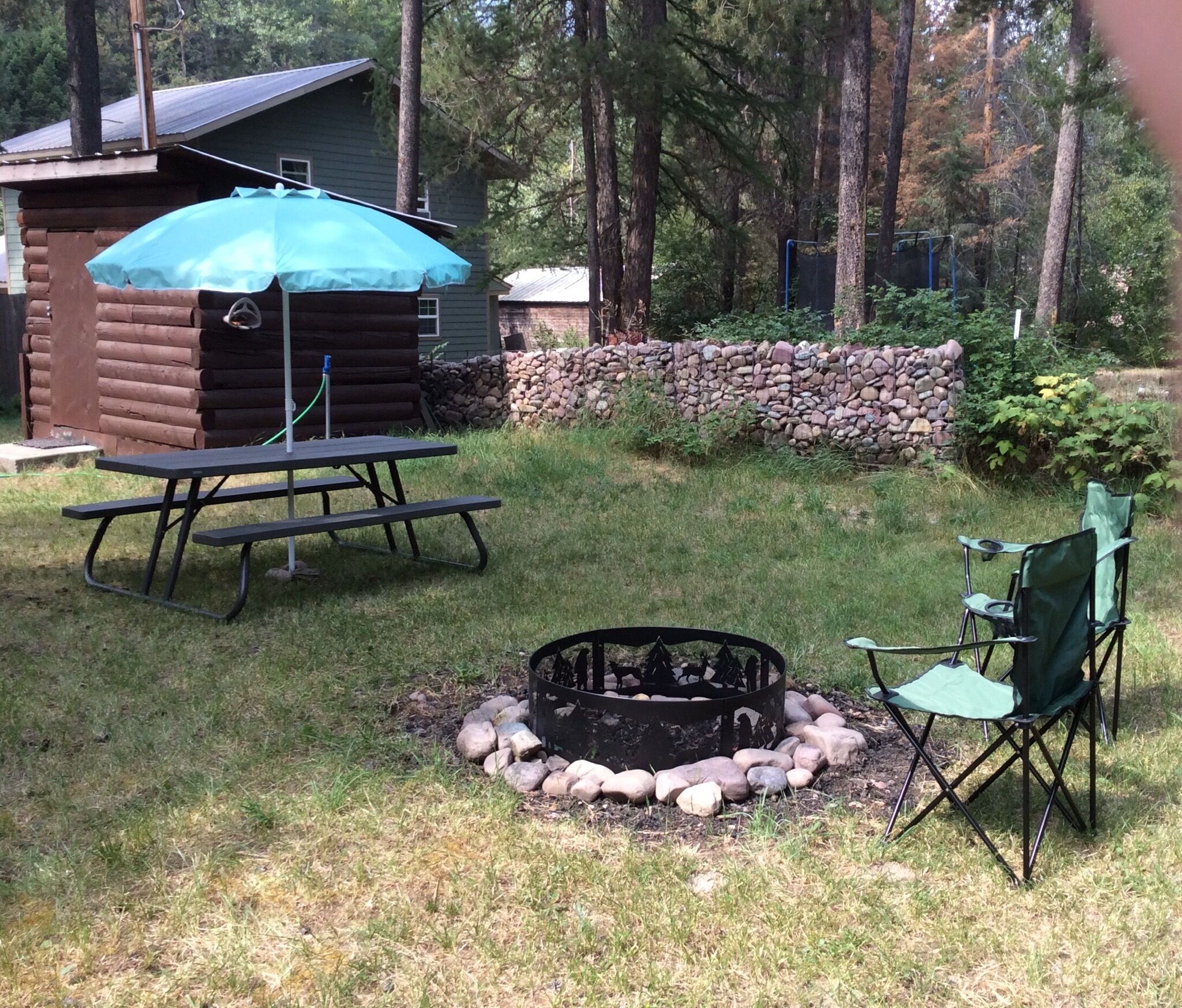 A backyard with a picnic table, a fire pit, and a covered grill.