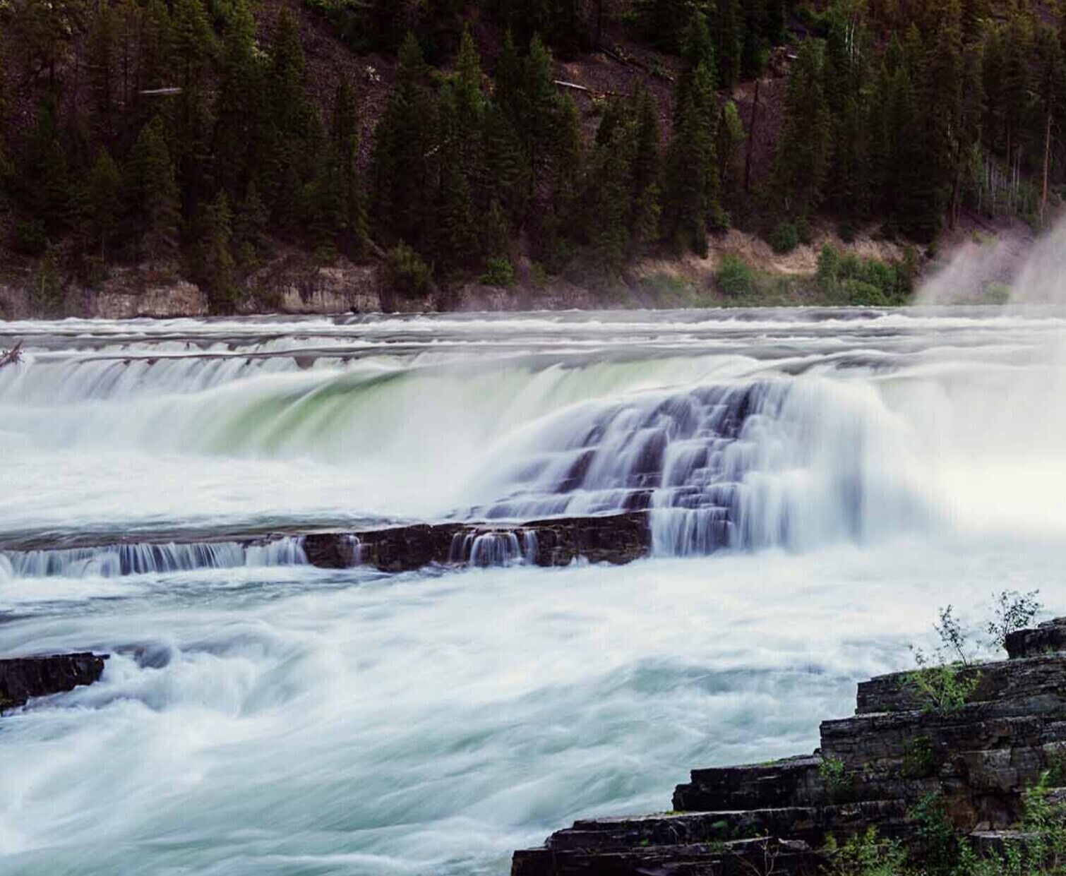 A waterfall cascading over a rocky ledge with dense forest in the background.