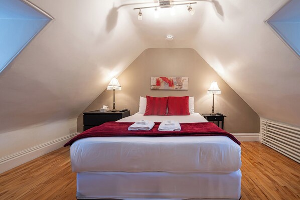Une chambre à coucher avec un grand lit, deux lampes de chevet, un plaid rouge et un tableau accroché au mur.