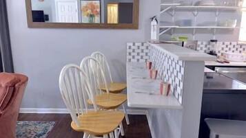 Une cuisine avec un plan de travail blanc, deux chaises blanches et un miroir au mur.