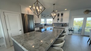 Una cocina moderna con una isla grande, electrodomésticos de acero inoxidable, iluminación colgante y vistas al exterior.