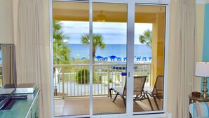 Quarto com vista para a praia, varanda com cadeiras e mesa com abajur.