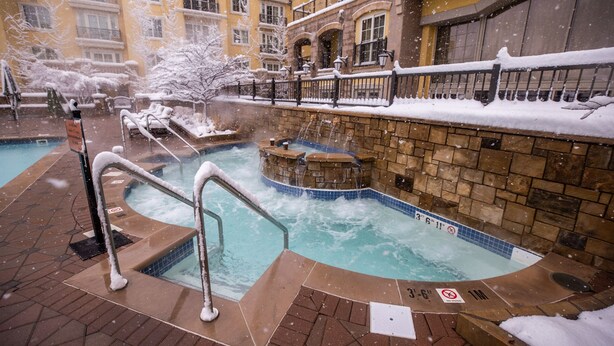 A heated outdoor swimming pool with a stone wall and a metal railing, surrounded by snow-covered buildings. - New Listing!! Ritz-Carlton At Vail Lion's Head Village!  Luxurious ski vacation! (Vail)