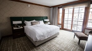 Een hotelkamer met een groot bed, een nachtkastje met lamp, een stoel en uitzicht naar buiten door een raam.