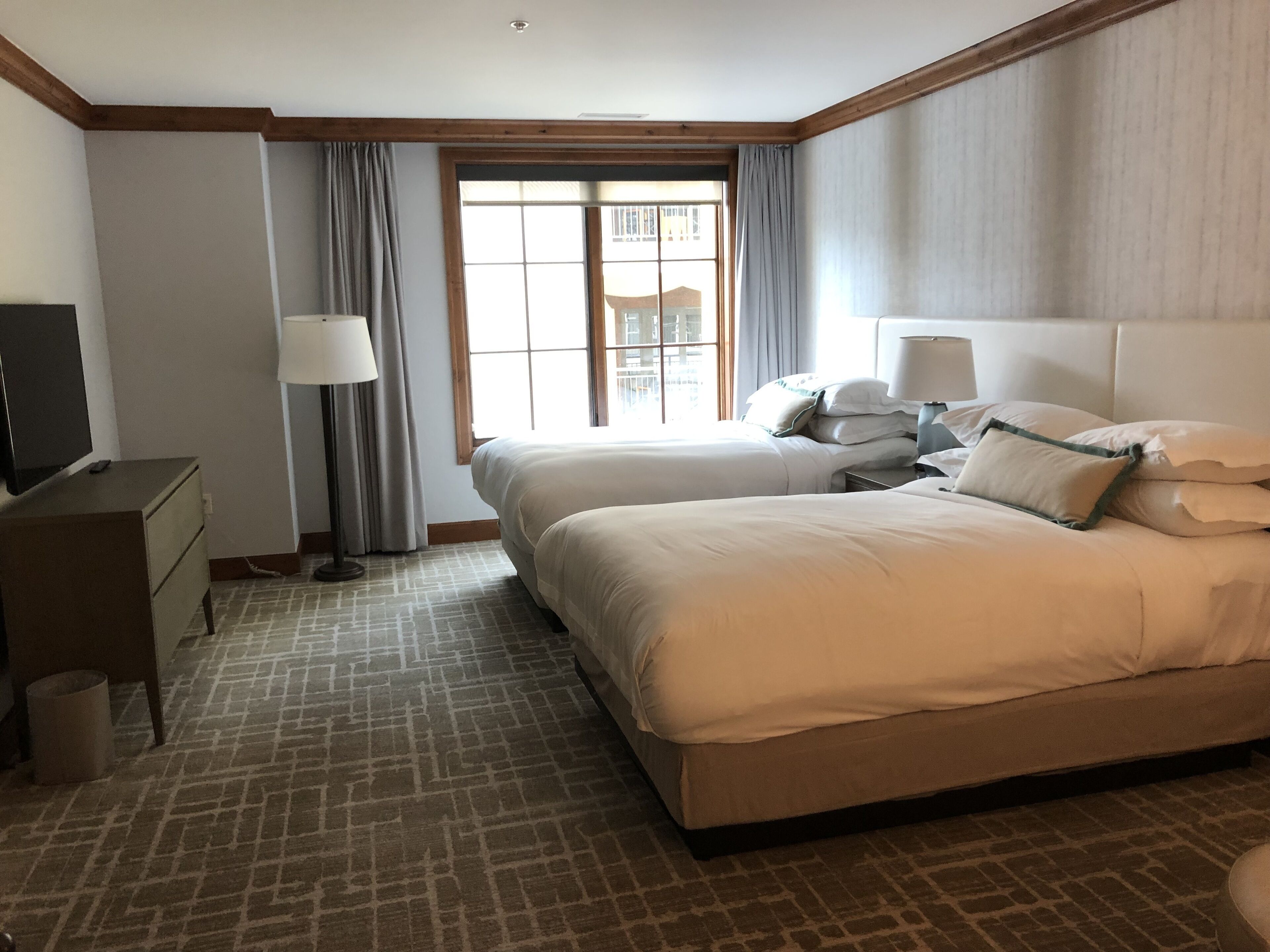 A hotel room with two beds, a desk, a TV, and a window with curtains.