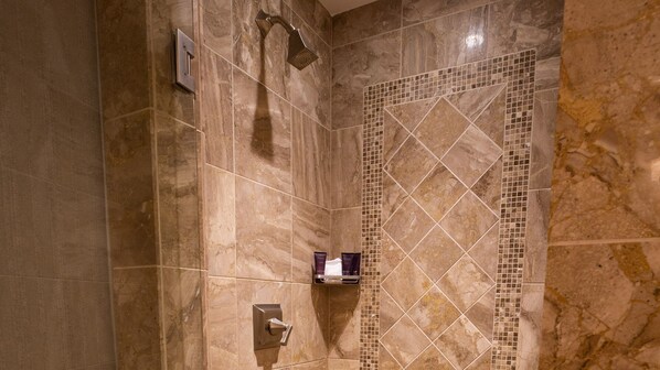Un baño moderno con paredes de mármol, ducha con cabezal de lluvia y un estante pequeño con artículos de aseo.
