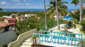 A pool area with a blue umbrella, palm trees, and a view of the ocean.
