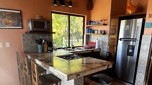 A kitchen with a central island, a refrigerator, and a window with a view of trees.