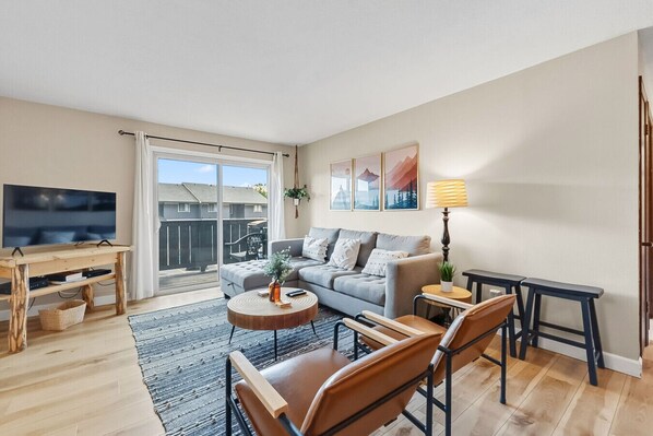 En moderne stue med sofa, sofabord, fjernsyn og en balkon.