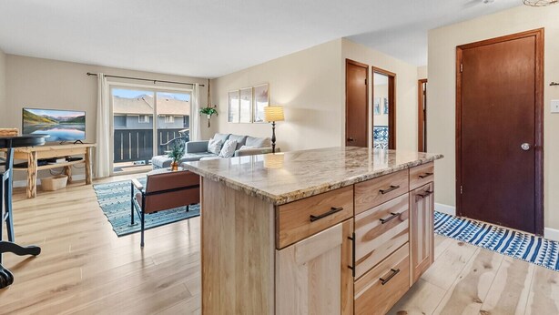 A modern kitchen with a marble countertop, wooden cabinets, and a dining area with a table and chairs.