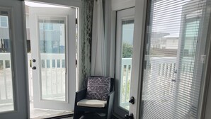 A room with a sliding glass door leading to a balcony, a cushioned chair, and a patterned rug. - Beautiful Cozy Beach Cottage, 1 block to beach, west of hotels, easy access (Pensacola)