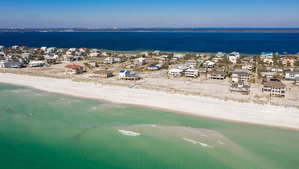 An aerial view of a coastal residential area with houses along the beachfront, clear blue water, and a distant bridge. - Beautiful Cozy Beach Cottage, 1 block to beach, west of hotels, easy access (Pensacola)