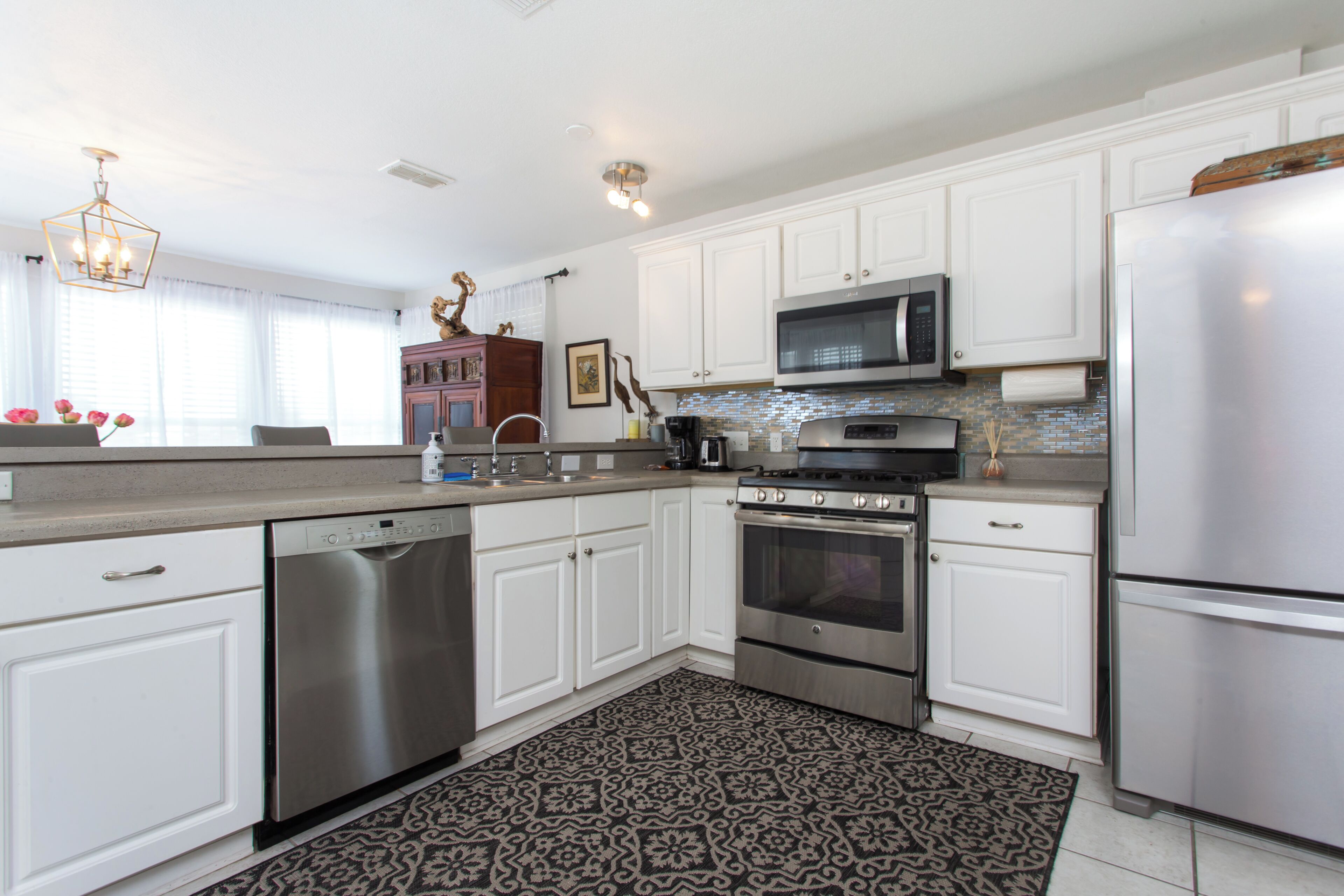 A modern kitchen with white cabinetry, stainless steel appliances, and a patterned rug.