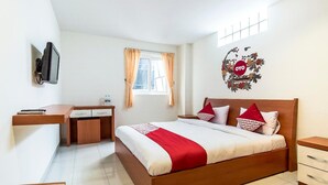 Quarto com cama, escrivaninha, cadeira, televisão e janela com cortinas.