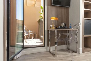 A modern hotel room with a glass door leading to a balcony, a small table with a lamp, and a TV mounted on the wall. - Oasis Hotel (Barcelona)