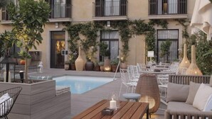 A poolside area with outdoor seating, a pool, and a building with balconies. - Oasis Hotel (Barcelona)