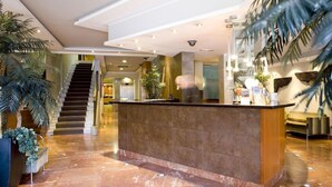 A hotel lobby with a marble reception desk, a staircase, and indoor plants. - Oasis Hotel (Barcelona)