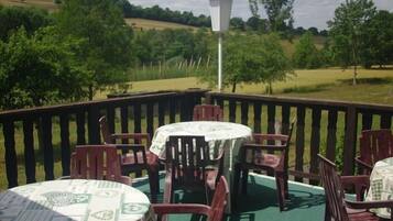 Een overdekt terras met tafels en stoelen, een lantaarnpaal en uitzicht op een groen landschap.