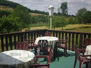 A covered outdoor seating area with tables and chairs, a lamp post, and a view of a green landscape. - Hotel Europa (Holsthum)