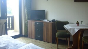 A hotel room with a bed, a desk with a computer, a chair, a table with a vase, and a window with curtains. - Hotel Europa (Holsthum)