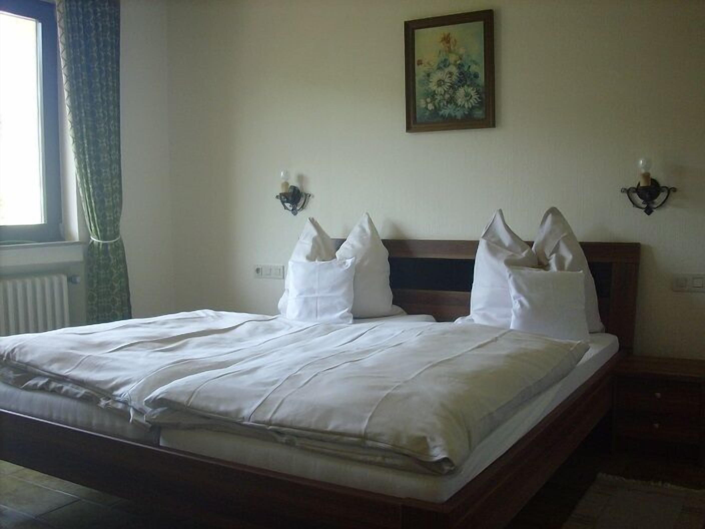 A neatly made bed with white linens, a wooden headboard, and two wall-mounted light fixtures.