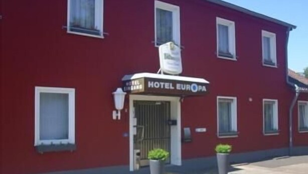 A red building with a sign reading 'HOTEL EUROPA' and a gated entrance. - Hotel Europa (Holsthum)