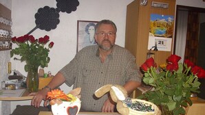 A man seated at a table with a vase of red roses, a basket with a heart-shaped decoration, and a framed picture on the wall. - Hotel Europa (Holsthum)