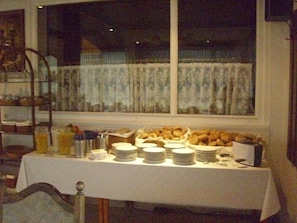 A breakfast buffet with plates, bowls, and a fruit basket. - Hotel Europa (Holsthum)