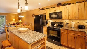 A kitchen with granite countertops, wooden cabinets, a black refrigerator, a stove, and a microwave. - Hi Country Haus Unit 1903 River view from private deck 2 bedroom modern interior (Winter Park)