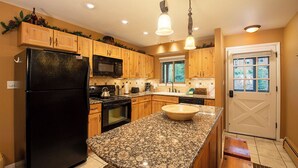 A kitchen with wooden cabinets, a black refrigerator, granite countertops, a sink, and a door with a window. - Hi Country Haus Unit 1903 River view from private deck 2 bedroom modern interior (Winter Park)