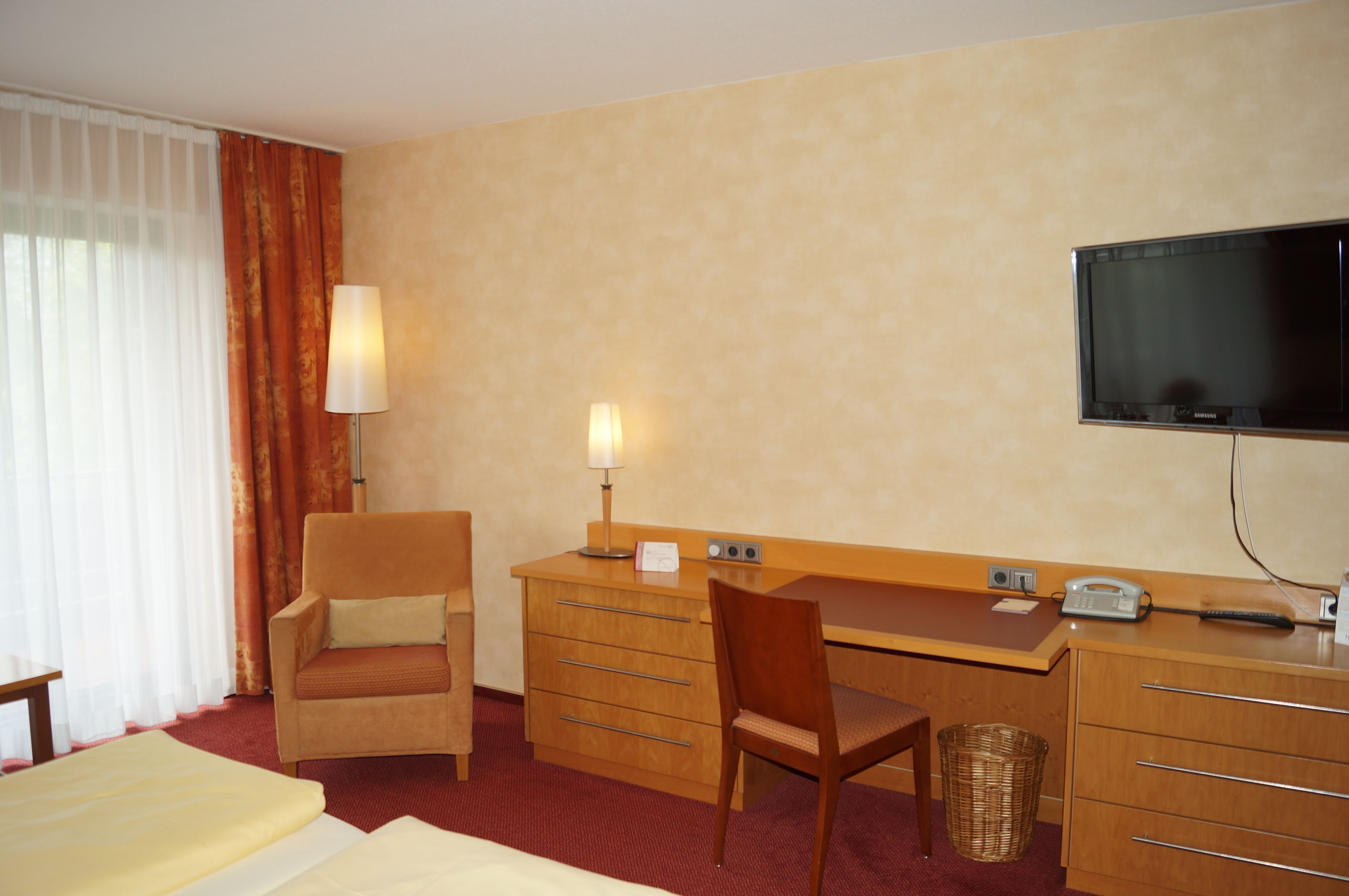 Ein Hotelzimmer mit einem Bett, einem Schreibtisch mit Stuhl, einem Fernseher, einer Lampe und einem Telefon.