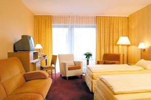 A hotel room with two beds, a sofa, a desk with a television, and two lamps. - Hotel an der Ilse (Lemgo)