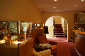 A hotel lobby with a reception desk, a staircase, and a seating area with a table. - Hotel an der Ilse (Lemgo)