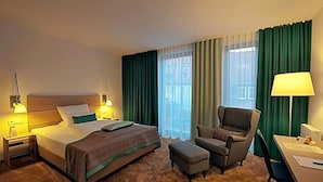 Une chambre d’hôtel comprenant un lit, une chaise, un pouf, un bureau et une lampe.