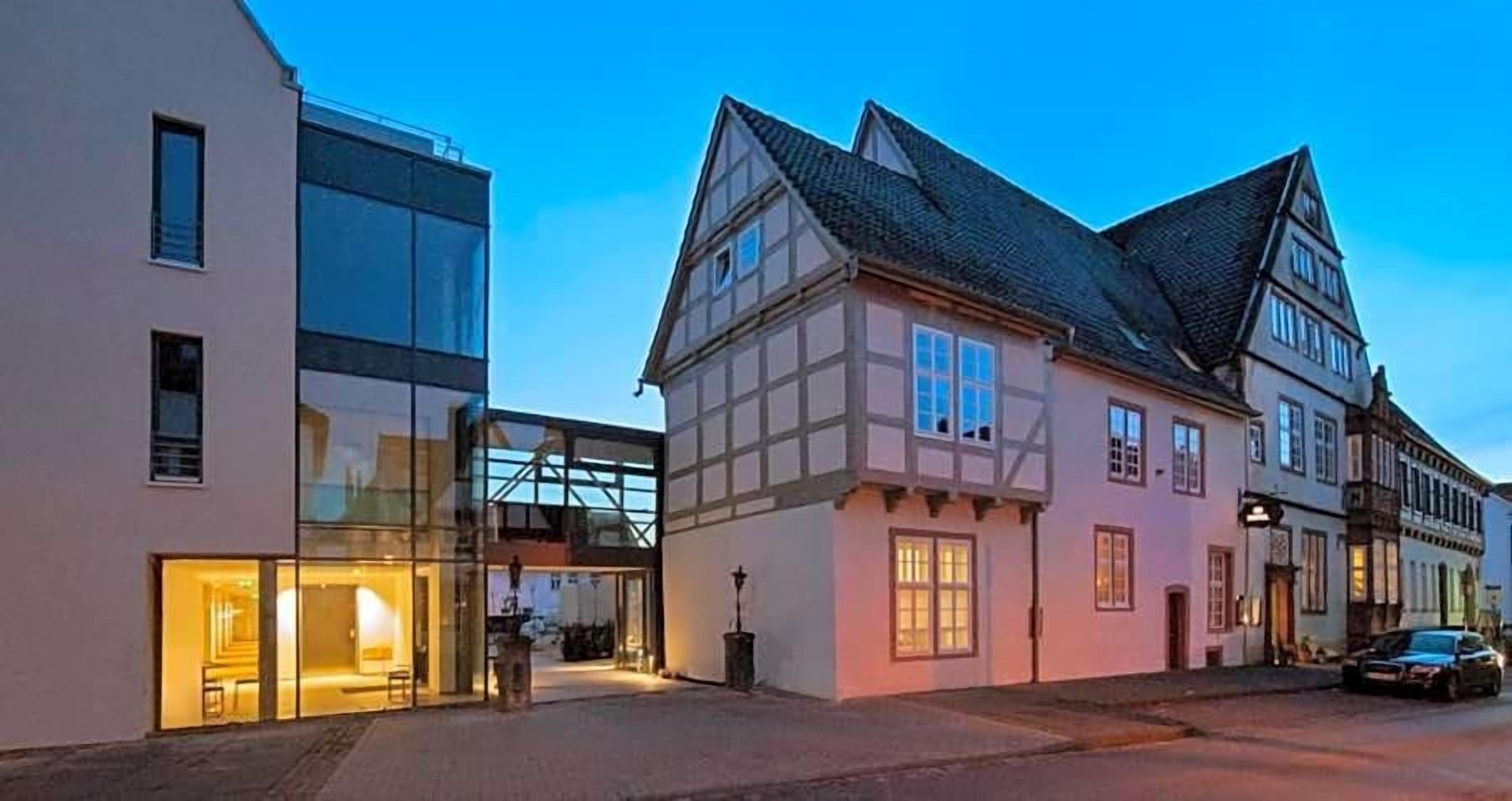 A traditional building with a modern glass extension, a car parked in front, and a clear sky.