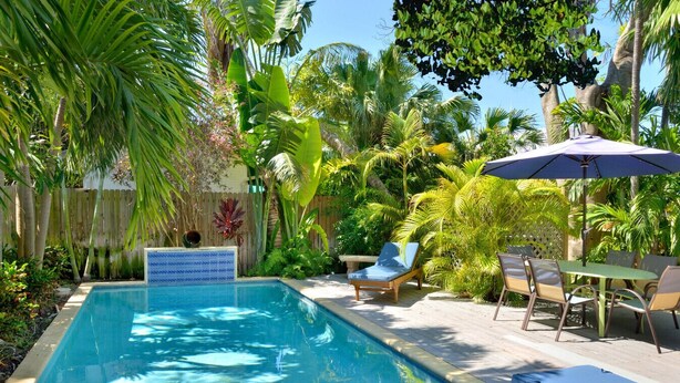 Ein rechteckiger Pool mit Fliesenrand, umgeben von Liegestühlen und einem Tisch mit Sitzgelegenheiten.