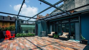A covered patio with a brick floor, red chairs, and a glass enclosure. - Sweethome37 (New Taipei City)
