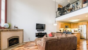 Ein modernes Wohnzimmer mit Kamin, einer Couch, einem Fernseher und einer Küchenzeile mit Holdekor und Geräten.