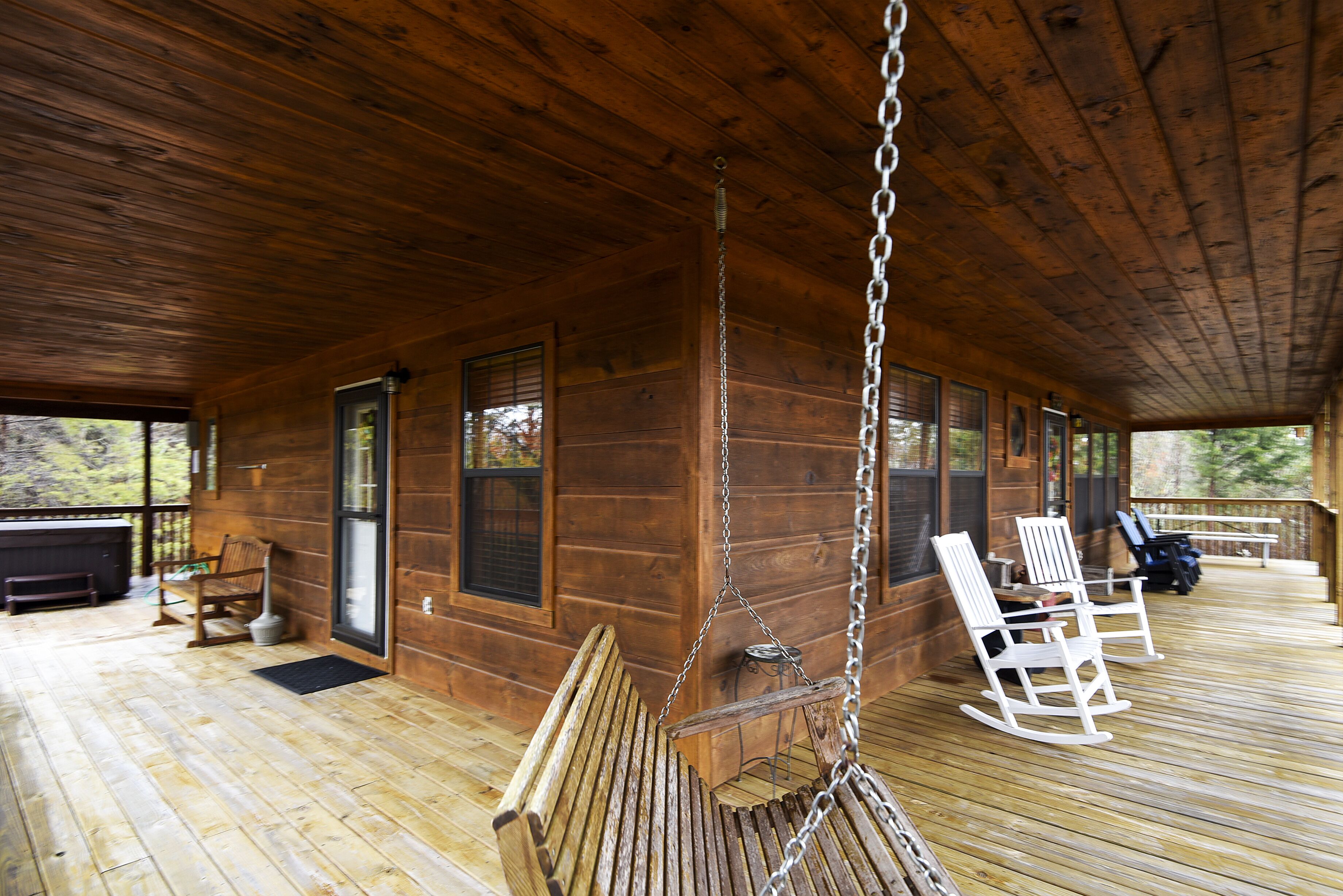 A wooden cabin with a porch, rocking chairs, and a swing.